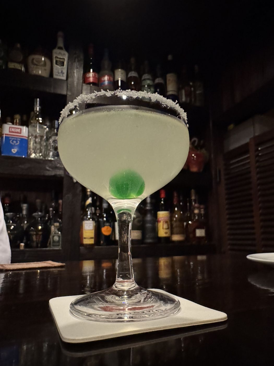 A margarita with a green cherry on a dark bar